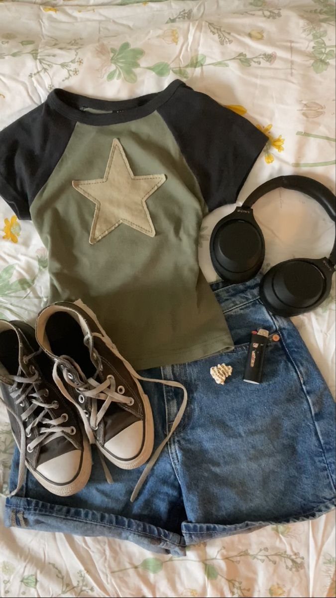 Denim shorts, a star graphic t-shirt, sneakers, and headphones laid out on a floral bedsheet.
