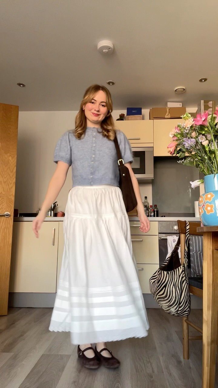 A woman wearing a light blue top and a long white tiered midi skirt.