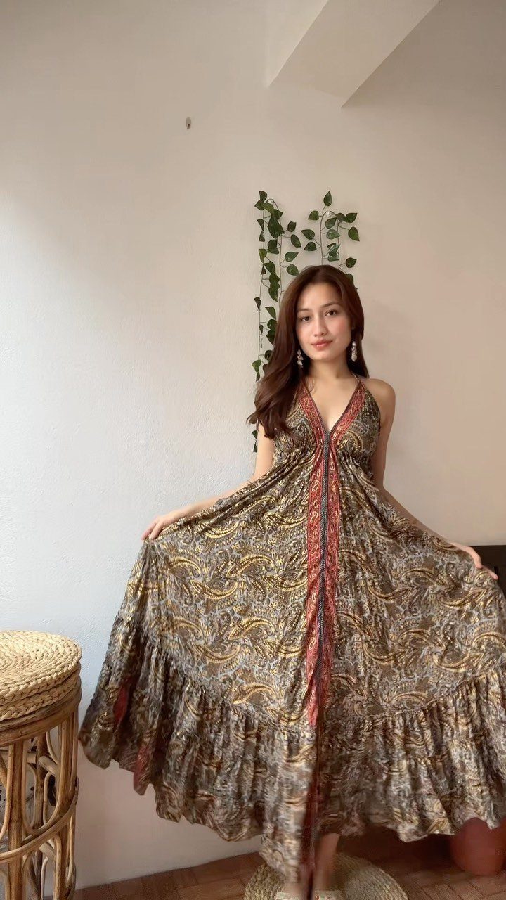 A woman posing in a patterned boho maxi dress against a white wall.