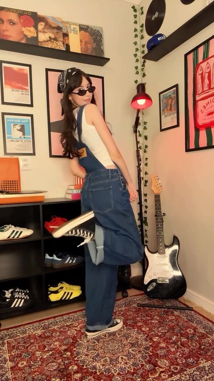 Woman in denim overalls and a white tank top posing in a music-themed room.