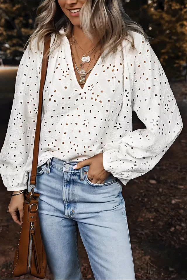Woman wearing a white eyelet blouse, light blue jeans, and layered gold necklaces outdoors.