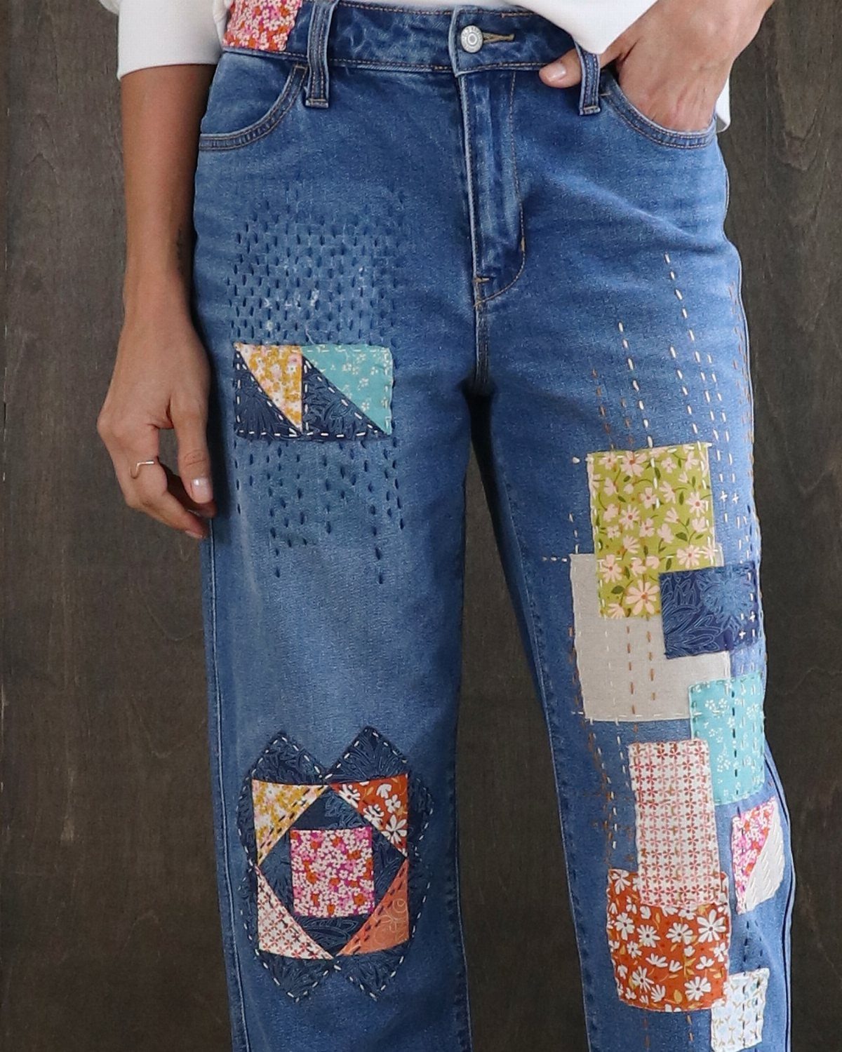 Blue denim jeans decorated with colorful patchwork fabric patterns on the legs.