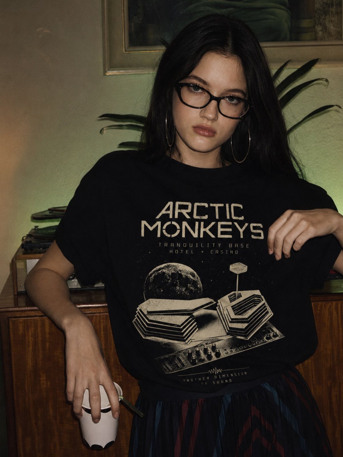 Young woman with glasses wearing a black Arctic Monkeys graphic t-shirt.