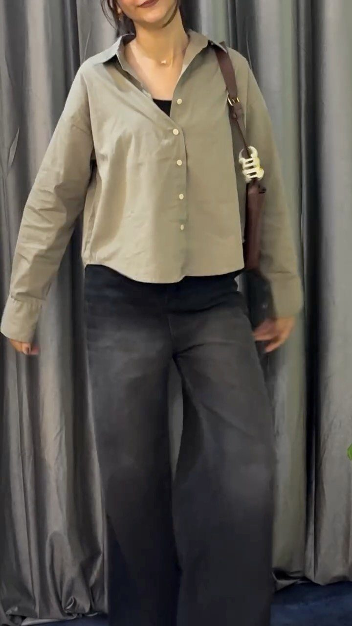 A person wearing an olive green button-down shirt and dark wide-leg denim jeans.