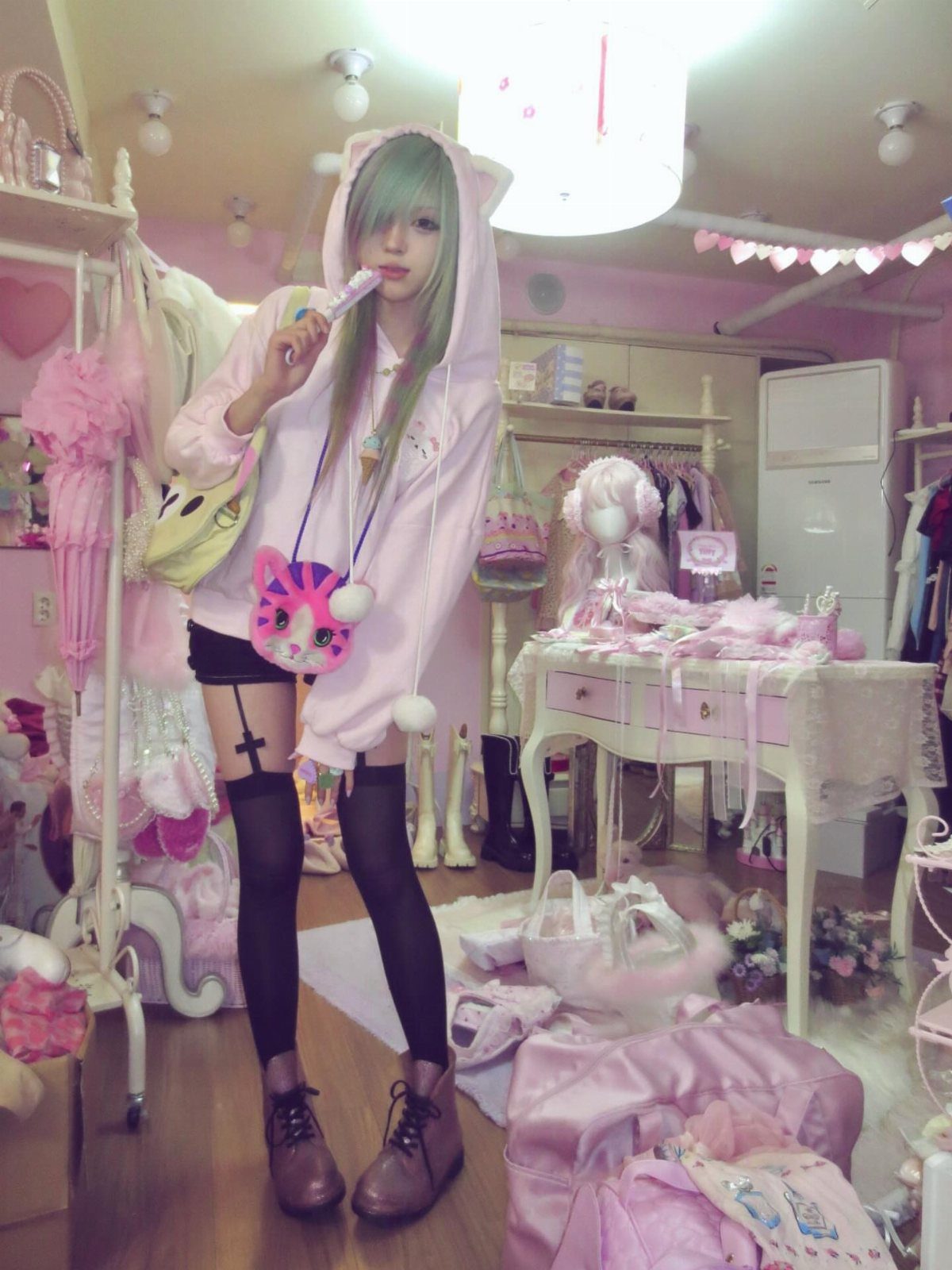 A girl in a pink animal ear hoodie, black shorts, and thigh-high stockings posing in a pink room.