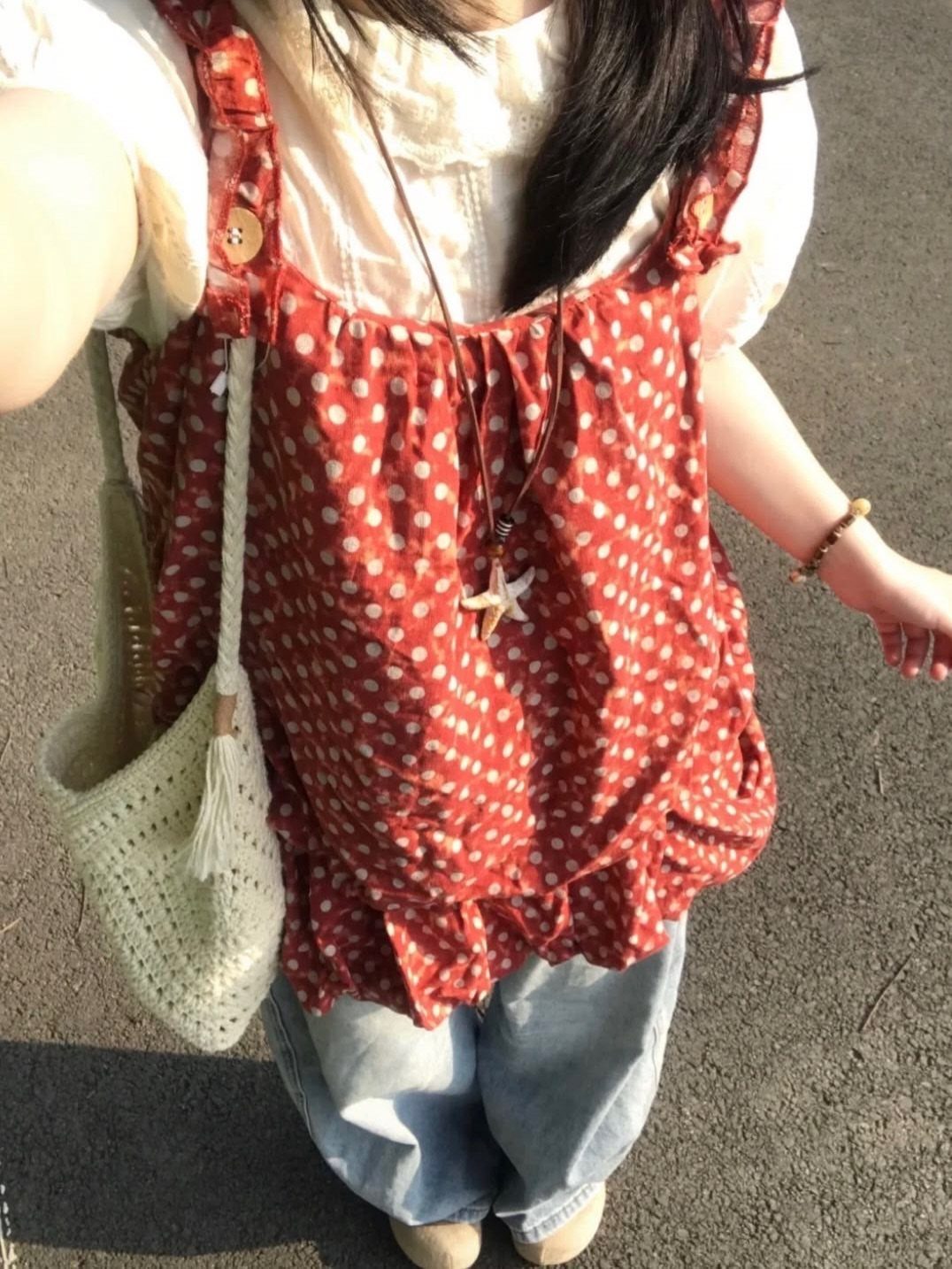 Person wearing a red polka dot ruffled top, white blouse, and light blue denim jeans.