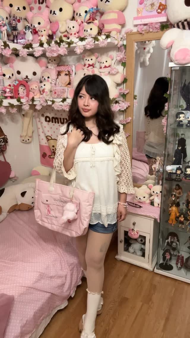 Young woman in a white lace top and denim shorts posing in a pink bedroom.