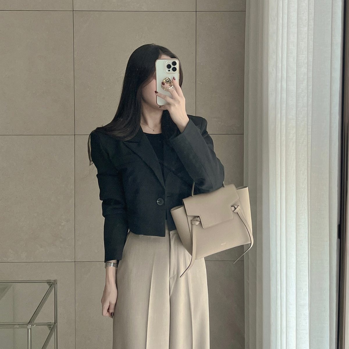 Woman in a black cropped blazer and beige wide-leg trousers holding a beige handbag.