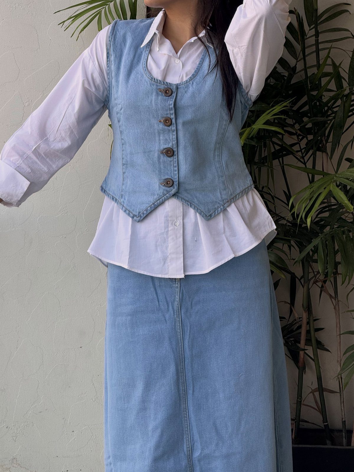 Person wearing a light blue denim vest over a white shirt and a denim skirt.
