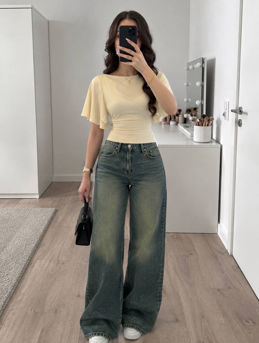 Woman in a cream top and wide-leg denim jeans posing for a mirror selfie.