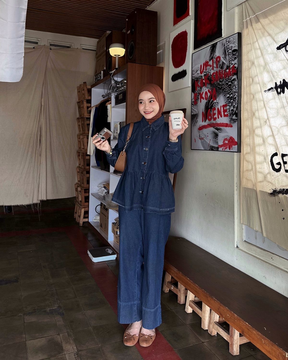 A woman in a denim peplum top and wide-leg trousers standing in a room.