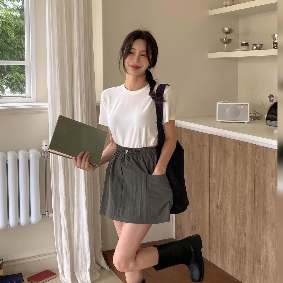 A smiling young woman wearing a white t-shirt and a grey short skirt posing indoors.