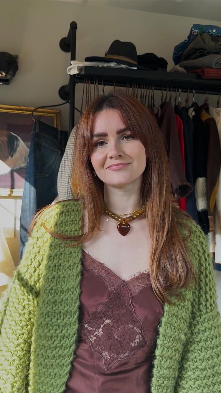 A woman wearing a brown lace camisole and a chunky green knit cardigan.