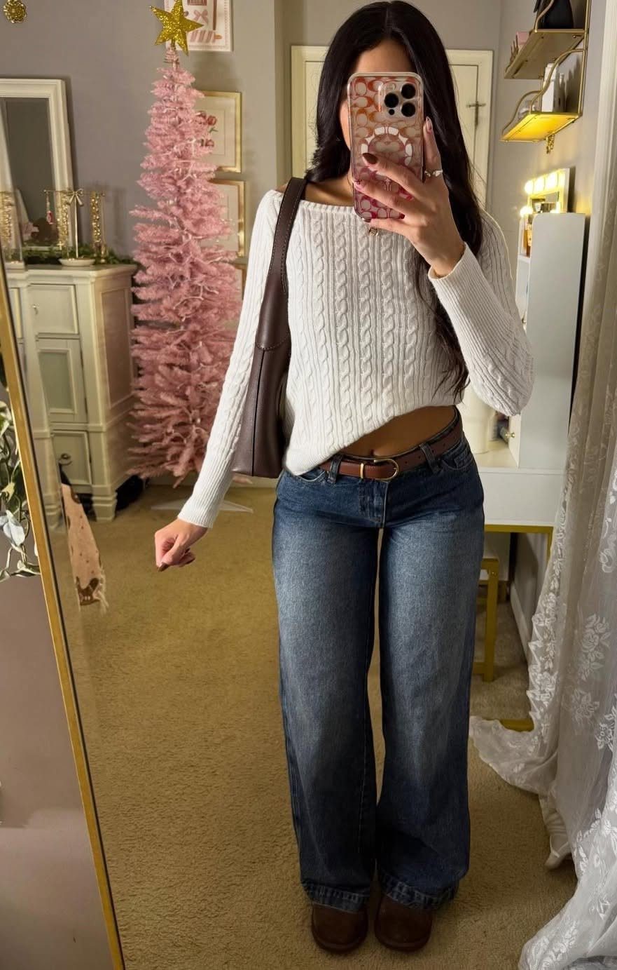 Woman in a white cable-knit sweater and blue wide-leg jeans posing for a mirror selfie.