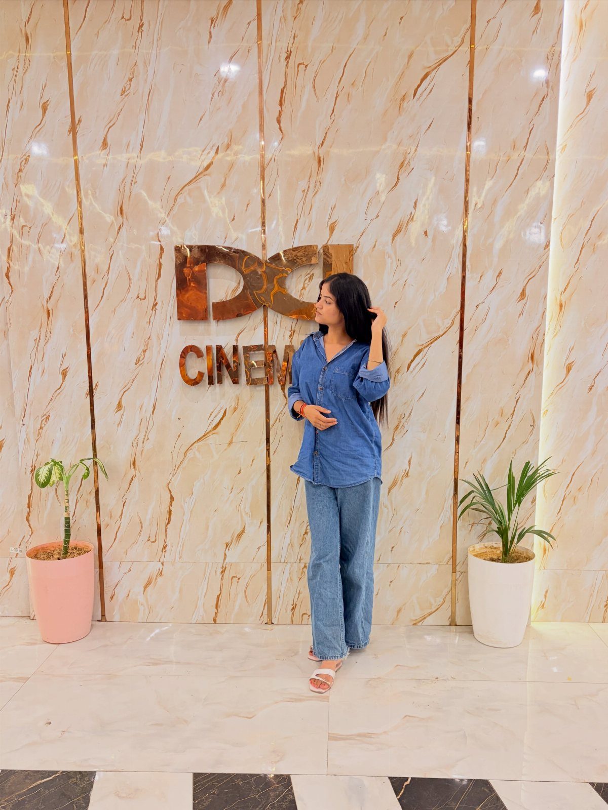 Woman wearing a blue denim shirt and wide-leg denim jeans standing in a cinema lobby.