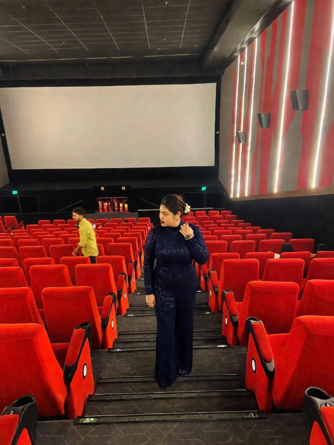 Woman wearing a sparkling dark blue jumpsuit standing in a movie theater aisle.