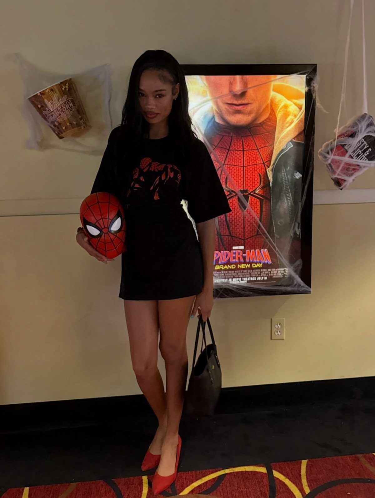A woman in a Spider-Man t-shirt dress holding a mask in front of a movie poster.