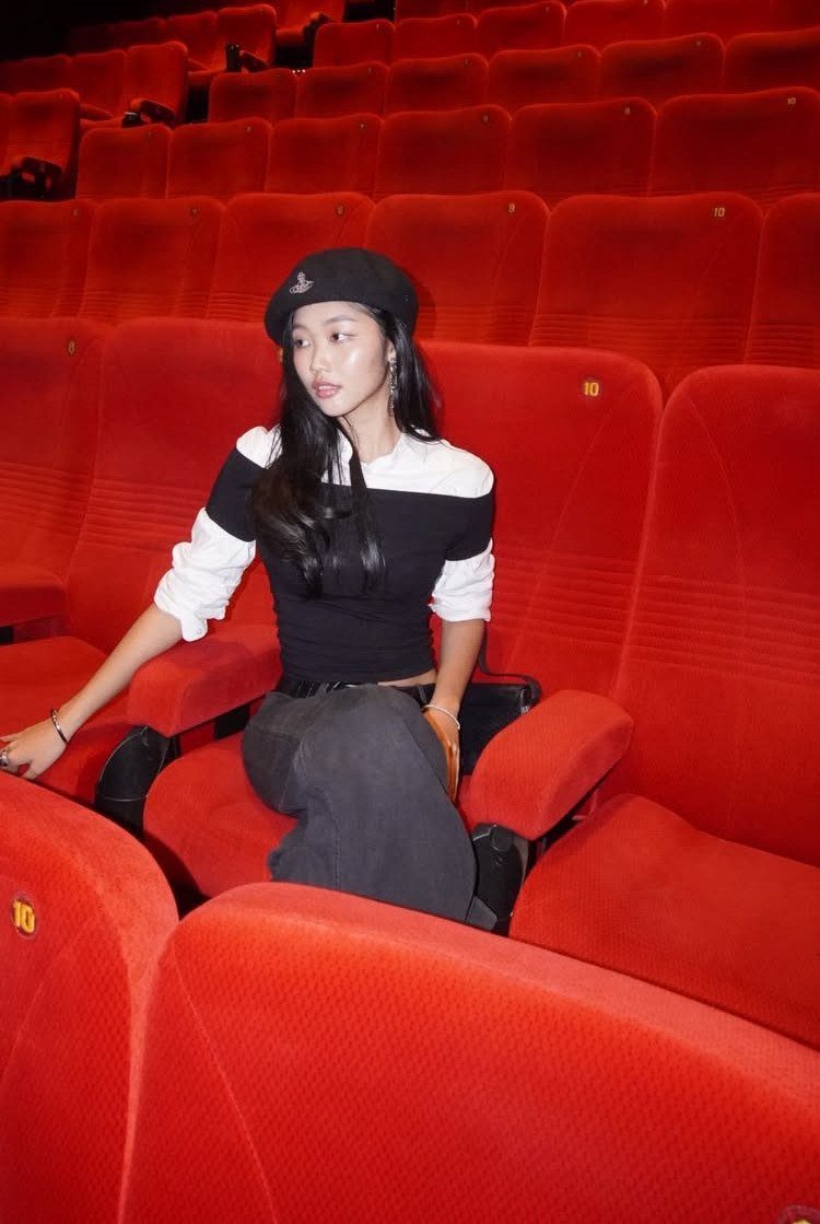 A woman in a black and white top and beret sitting in red theater seats.