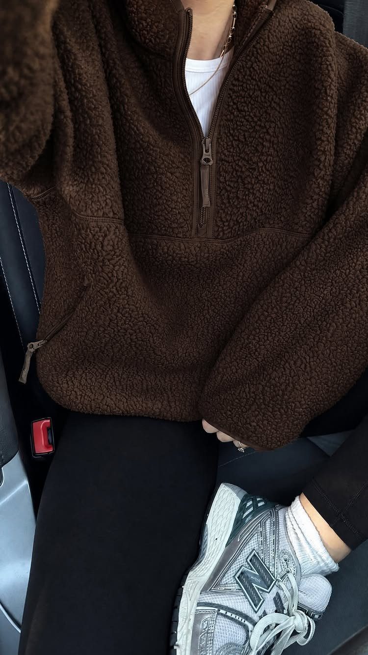 Person wearing a brown textured fleece quarter-zip pullover and black pants while sitting in a car.