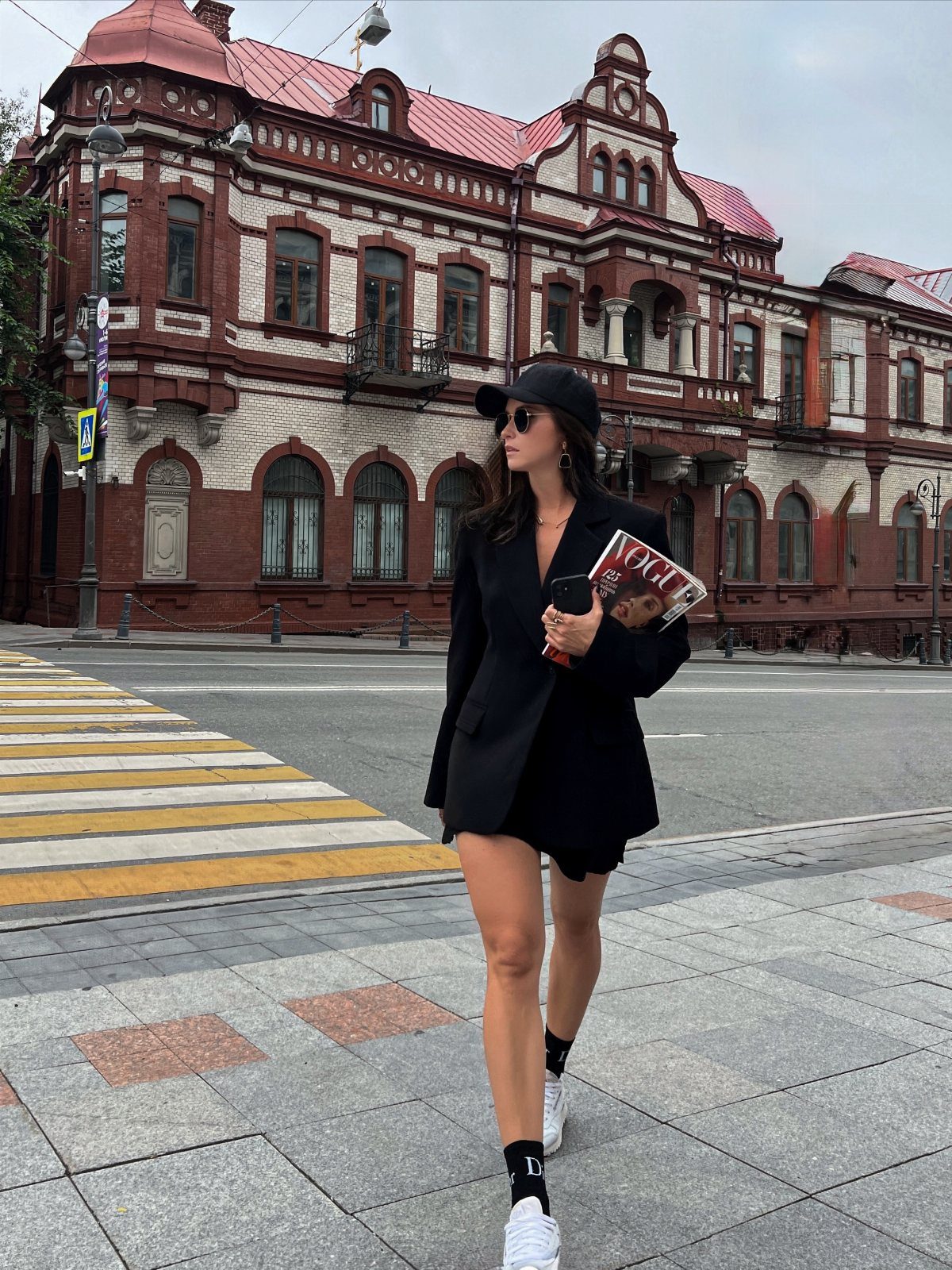 Woman walking in a city wearing a black oversized blazer, minidress, and white sneakers.