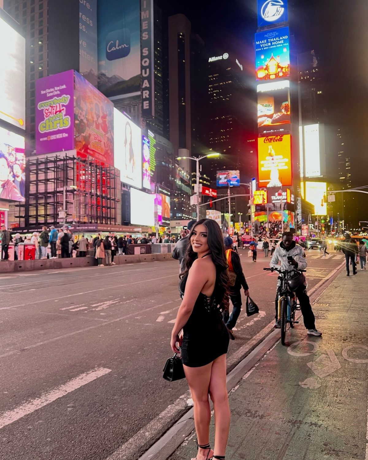 A woman wearing a black mini dress posing in Times Square at night.