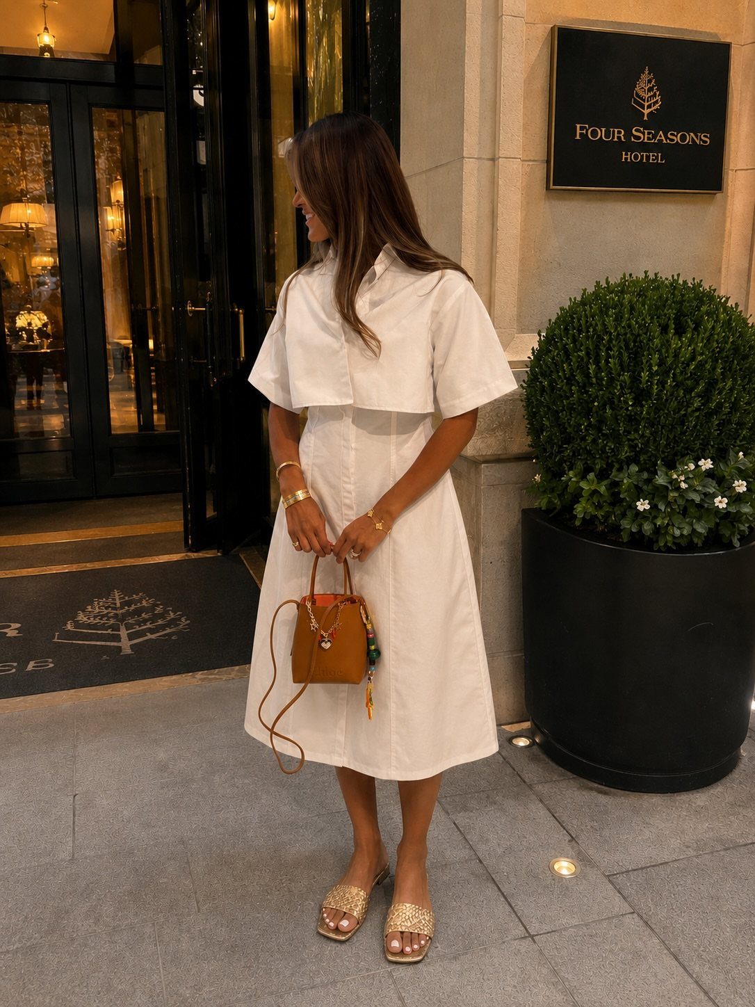 Woman in a white midi dress and sparkly sandals standing outside a hotel entrance.