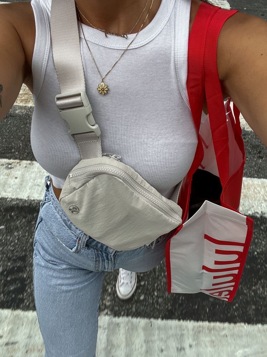 A person wearing a white tank top and light blue jeans with a beige crossbody bag.