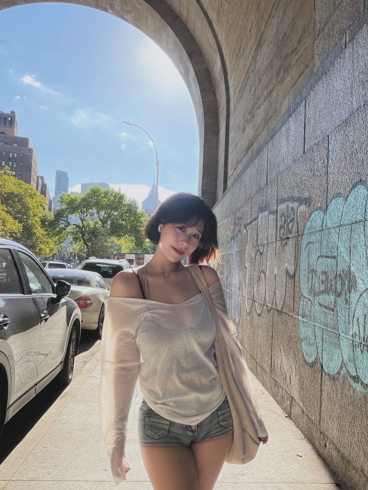 A woman wearing a light top and denim shorts posing under a city archway.
