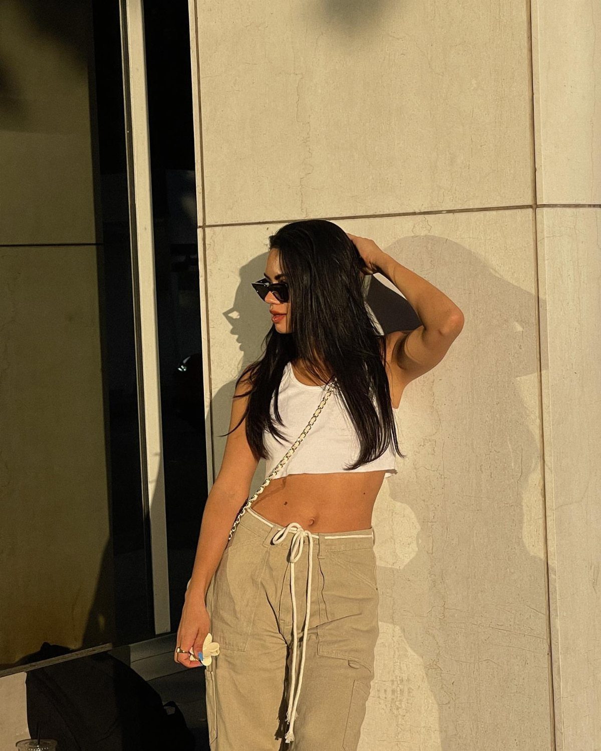 Woman wearing a white cropped tank top and beige cargo pants against a wall.