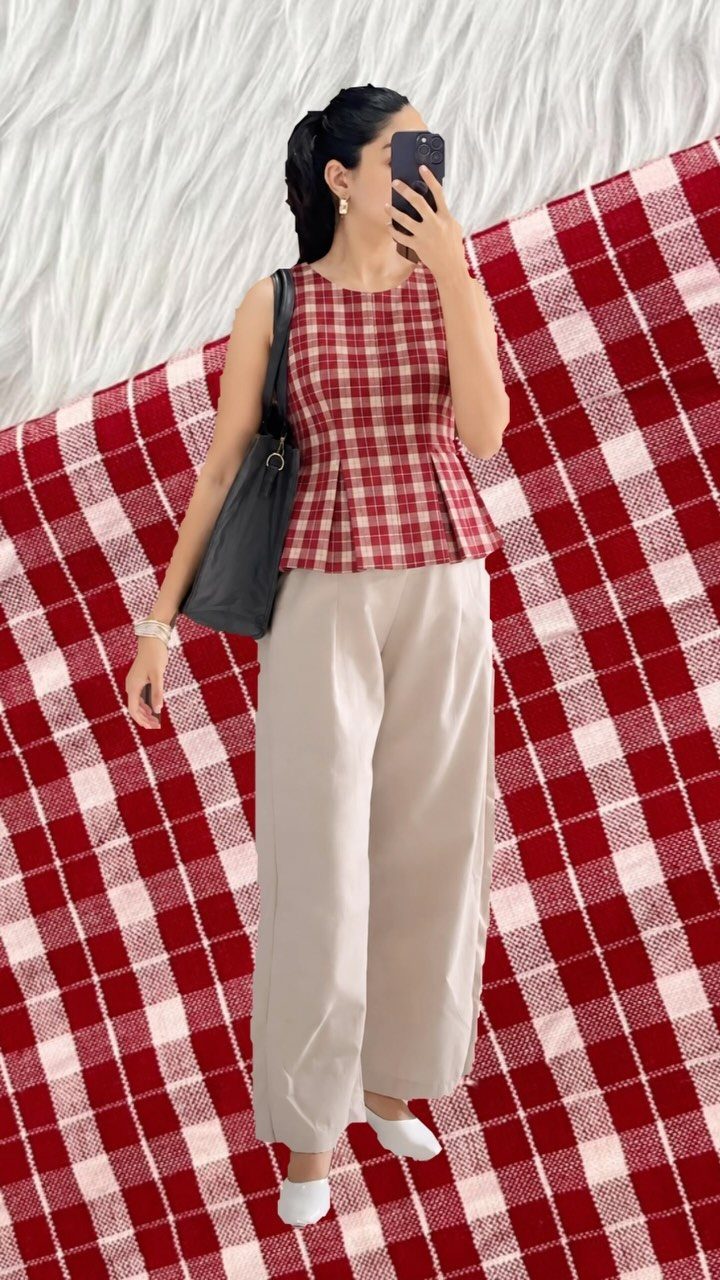 Woman wearing a red gingham peplum top and beige wide-leg trousers standing on a checkered blanket.