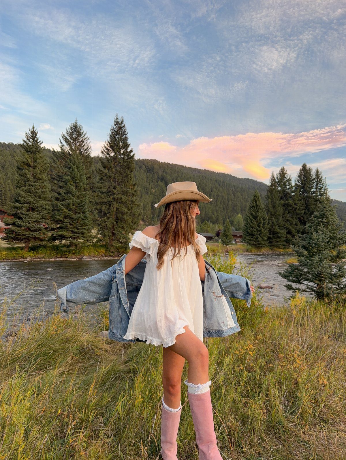 Woman in a white mini dress and pink boots wearing a tan hat in a field.