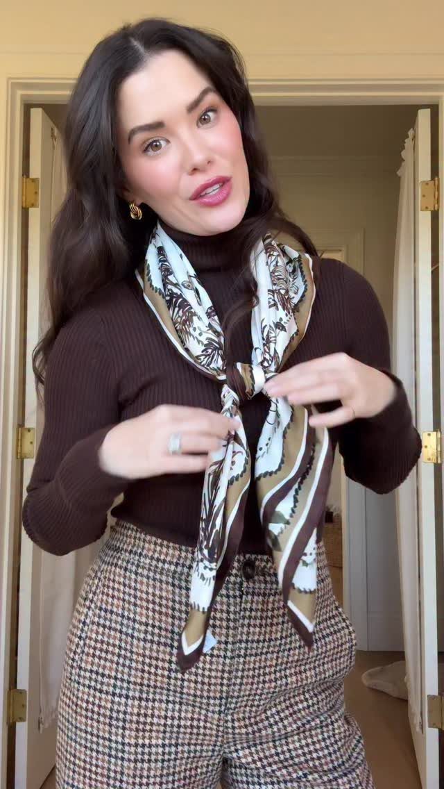 A woman wearing a brown turtleneck, patterned trousers, and a decorative silk scarf.