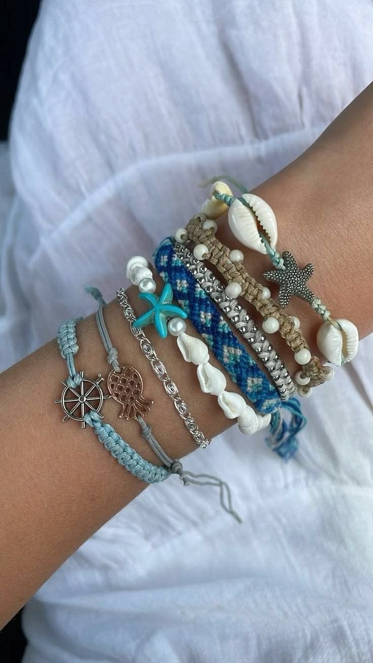 Multiple colorful summer bracelets with seashell and starfish charms on a person's wrist.
