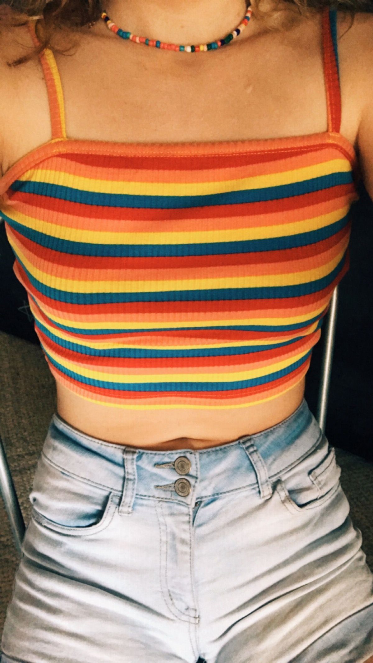 A person wearing a colorful striped cropped tank top and light denim shorts.