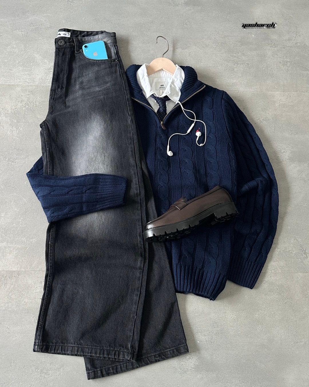Flat lay of navy cable-knit sweater, white shirt, tie, grey denim trousers, and brown loafers.