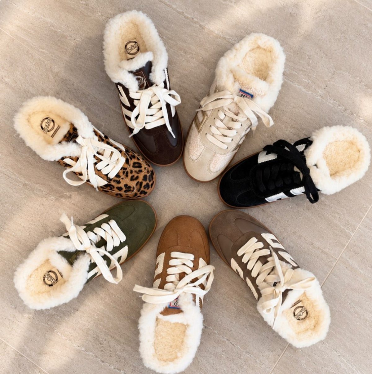 Six pairs of sneakers with white shearling linings arranged in a circle on a stone floor.