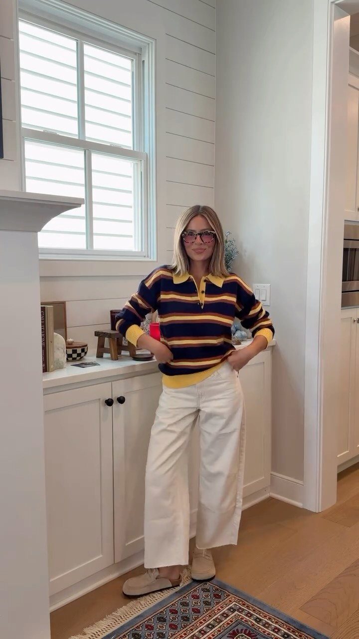 Woman wearing a striped rugby shirt layered over a yellow shirt and white wide-leg trousers.