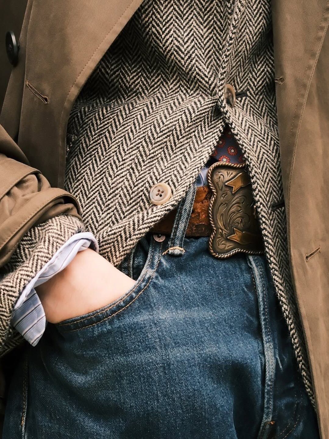Person wearing high-waisted vintage denim jeans with a herringbone waistcoat and tan trench coat.