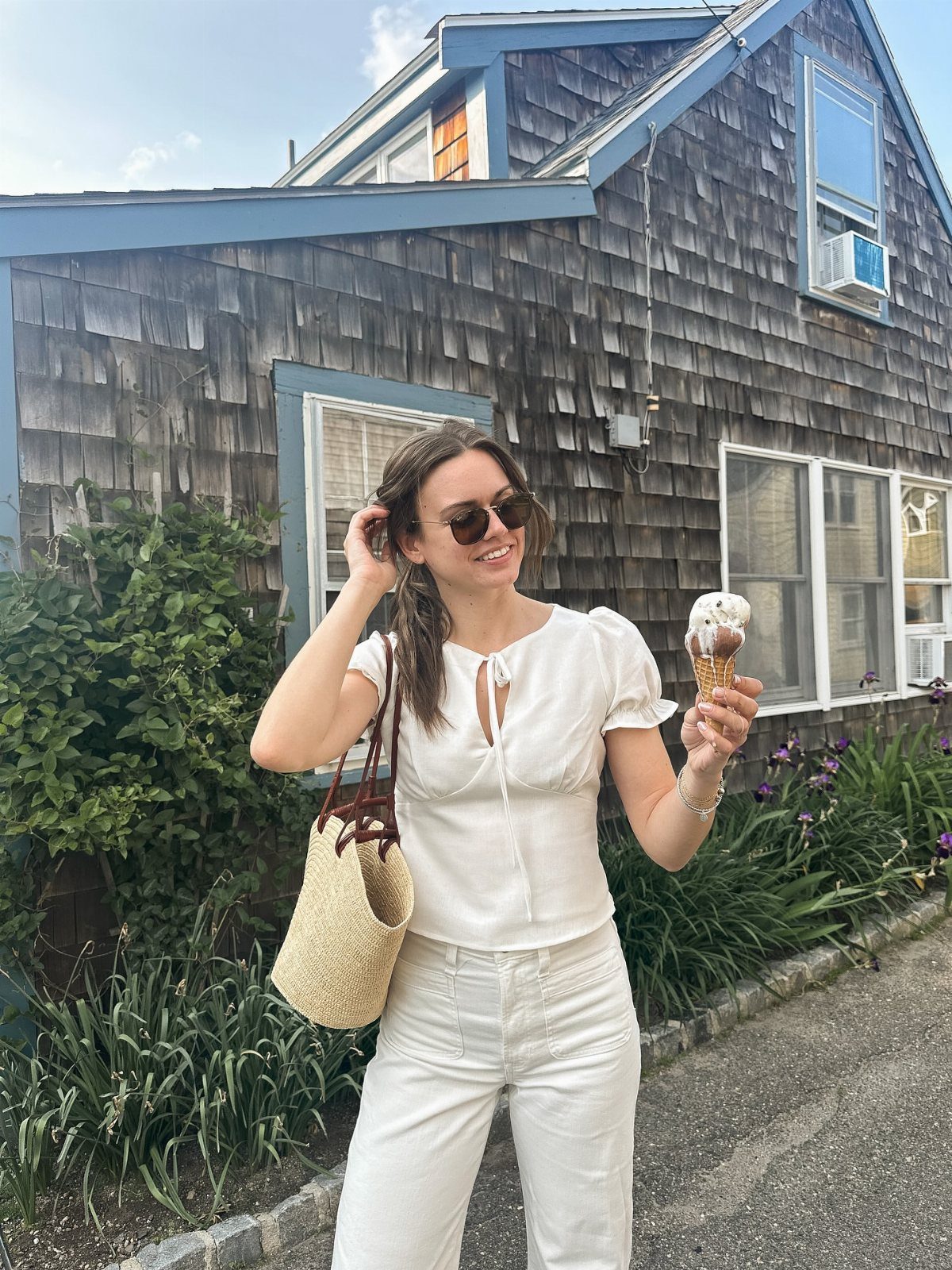 A smiling woman in white summer clothing holding an ice cream cone outdoors.