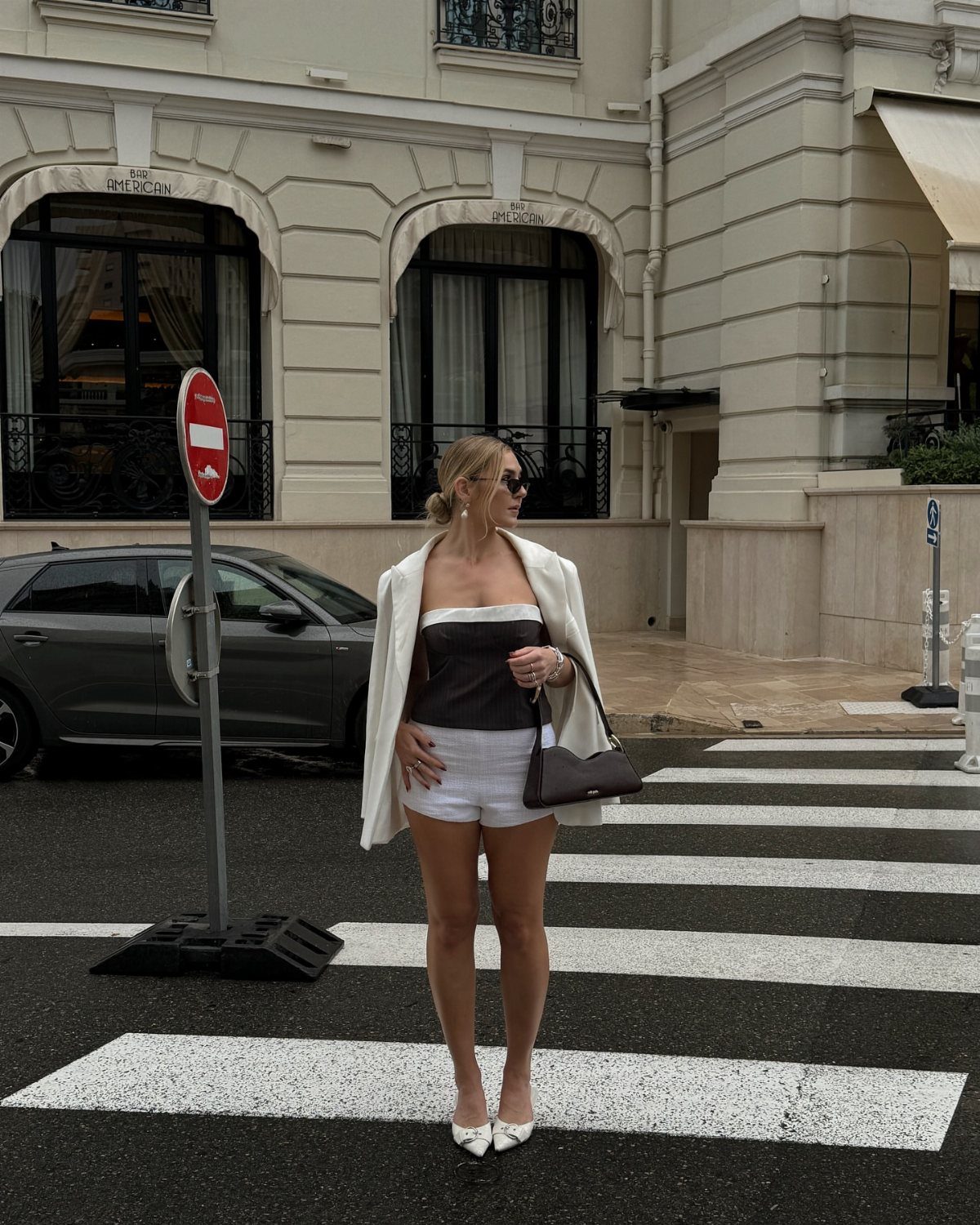 Woman in a white blazer and white structured shorts standing on a city crosswalk.