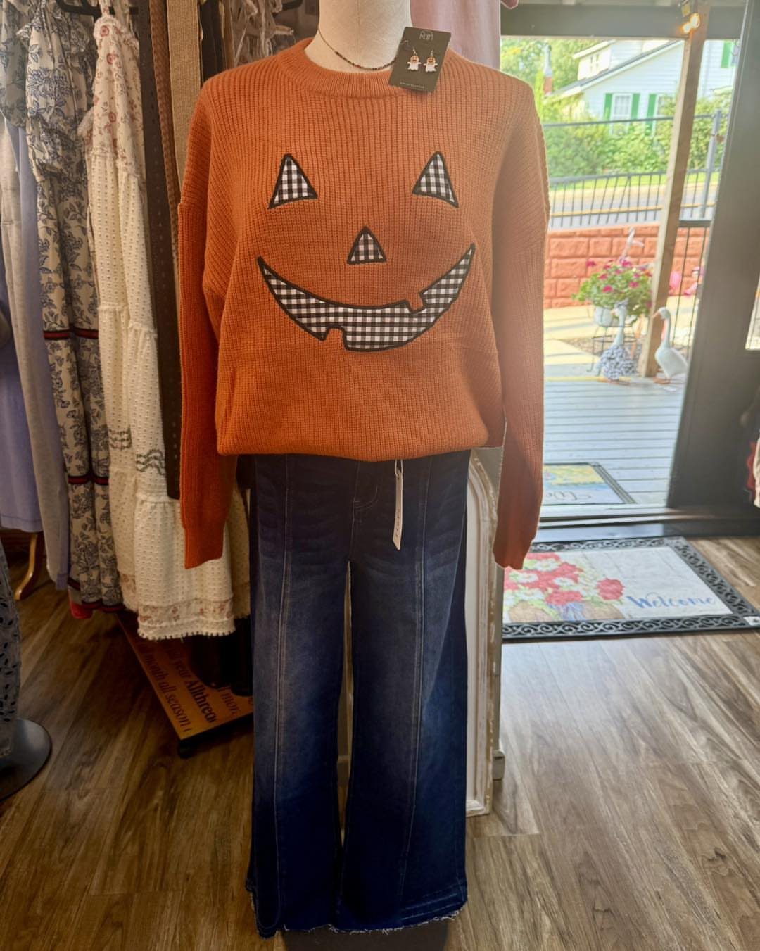 Mannequin wearing an orange pumpkin sweater and dark blue wide-leg denim jeans.