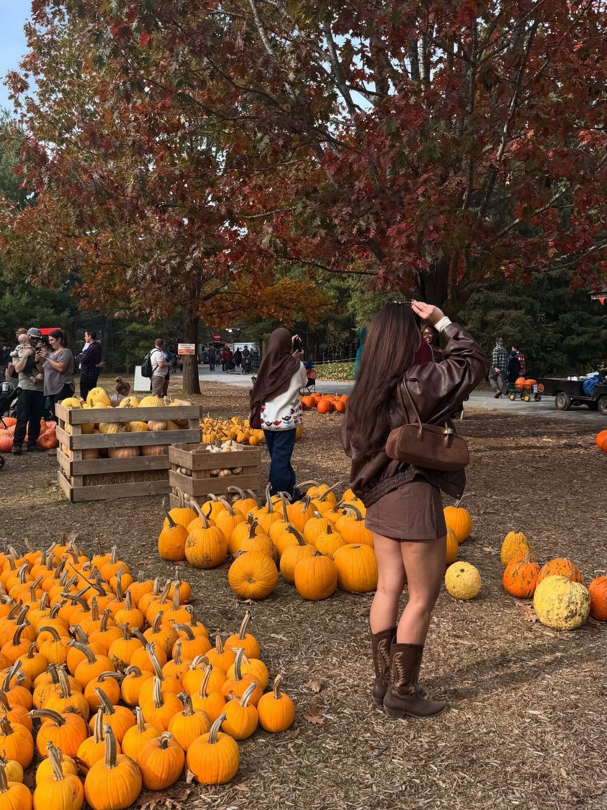 Woman wearing a brown monochrome outfit standing in a field of orange pumpkins.