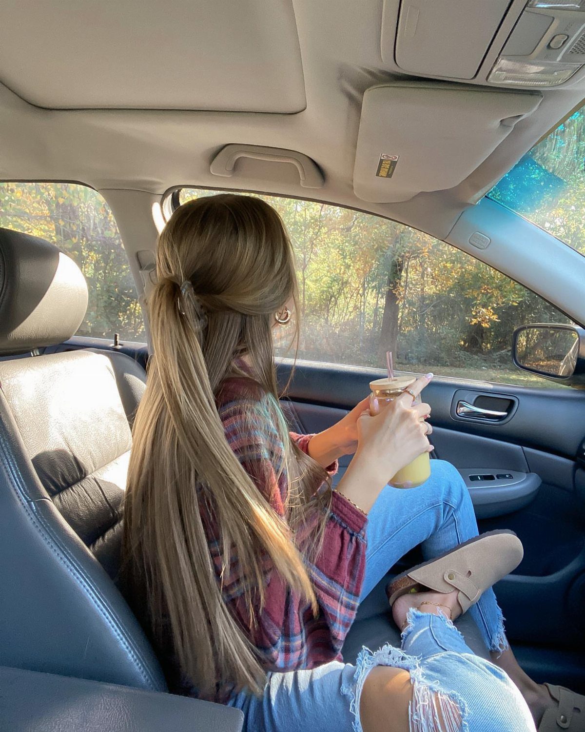 Woman in a plaid flannel shirt and ripped jeans sitting in a car passenger seat.