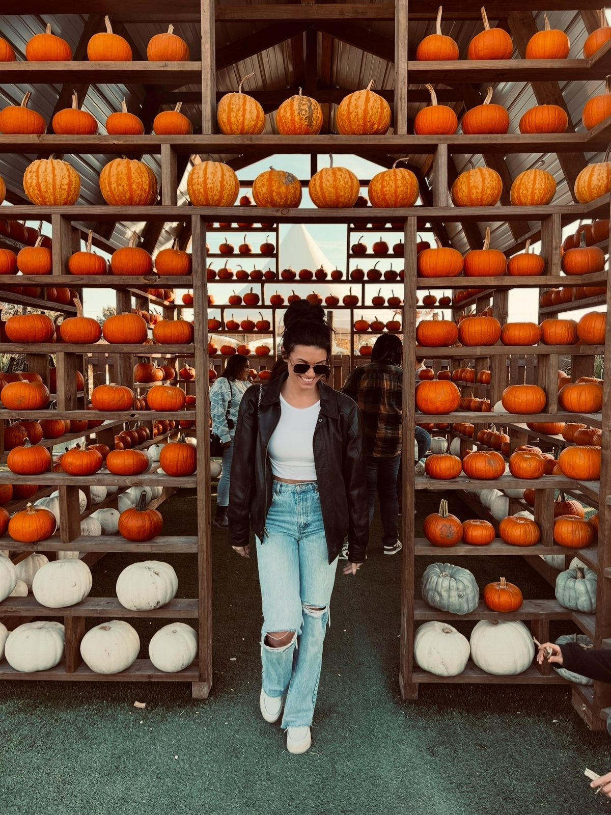 Woman wearing a black leather jacket and ripped light blue denim jeans walking through a pumpkin display.
