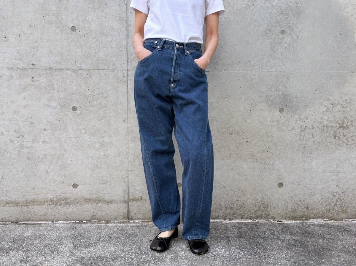 A person wearing high-waisted wide-leg blue denim jeans and a white t-shirt against a concrete wall.
