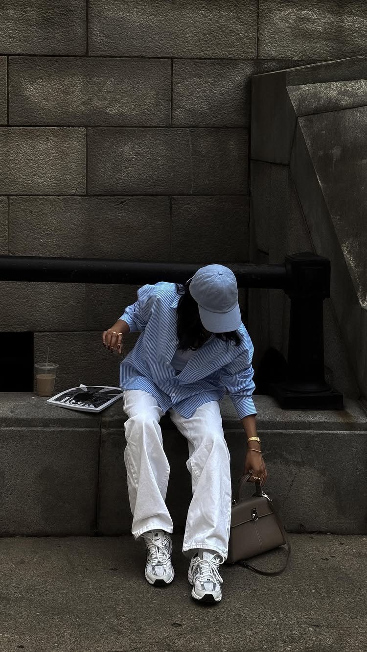 Person in a blue striped shirt and white wide-leg pants sitting on a stone ledge.