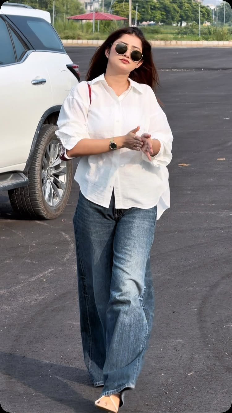 A woman wearing a white shirt and baggy blue denim jeans walking outdoors.