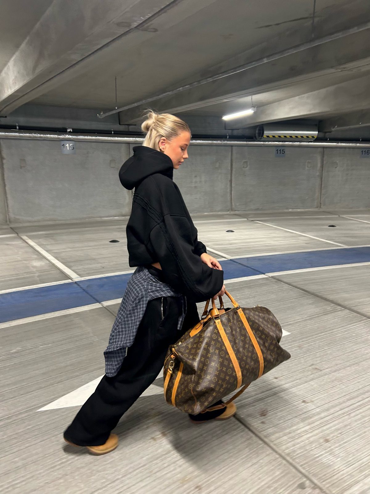 Woman walking in a parking garage wearing a black oversized hoodie and wide-leg pants.