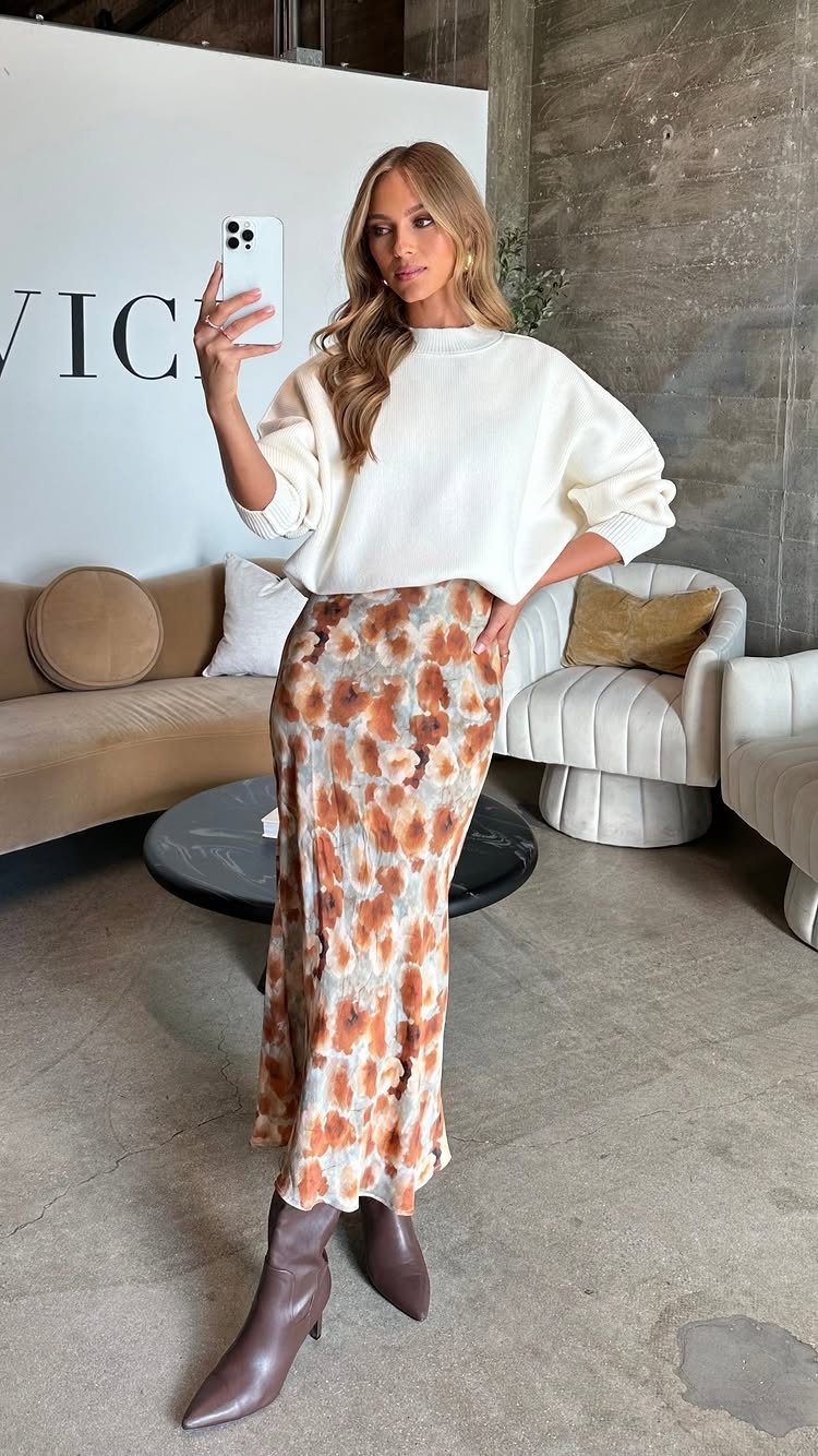 Woman in a white sweater and patterned satin skirt posing for a mirror selfie.