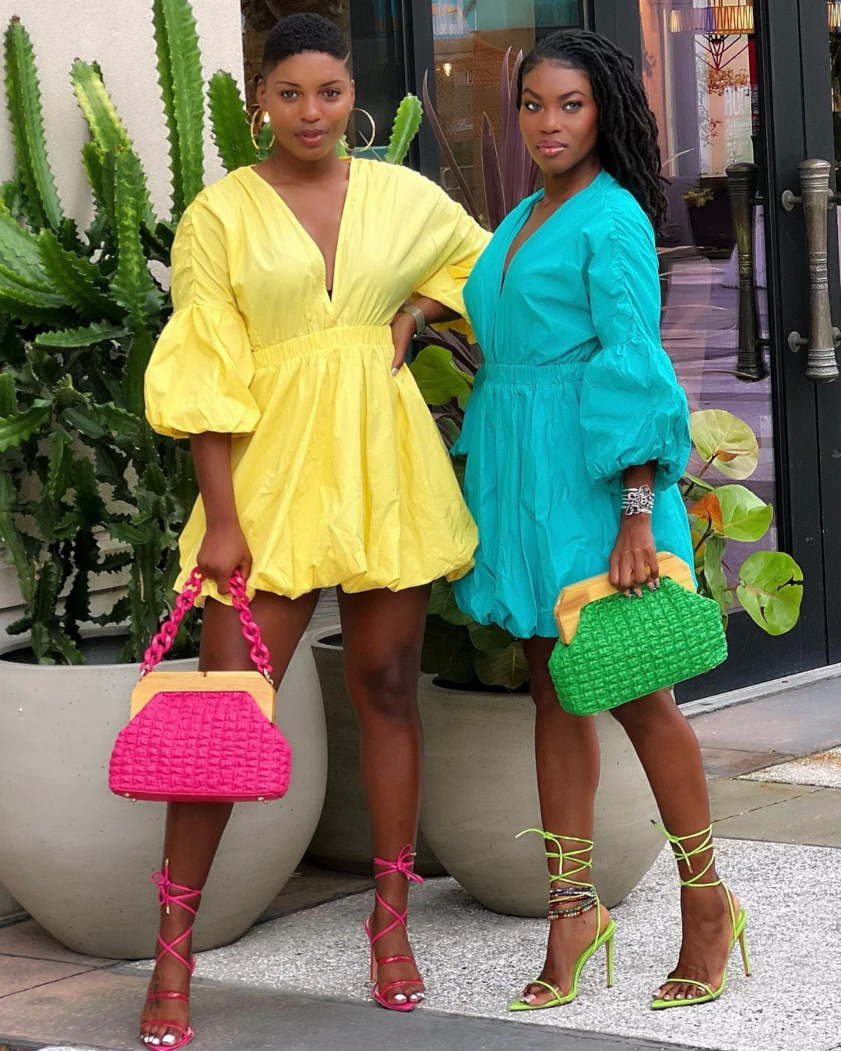 Two women posing in bright yellow and teal rompers with colorful strappy high heels.